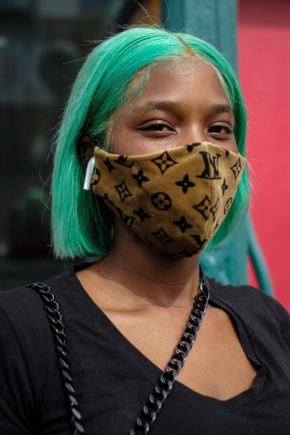 person with green hair and apple airpod wears golden Louis Vuitton printed mask